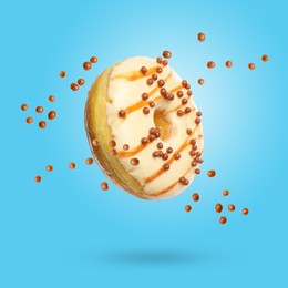 Image of Sweet tasty donut with crispy balls falling on light blue background