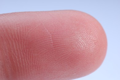 Photo of Finger with friction ridges on light blue background, macro view