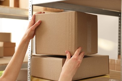 Photo of Post office worker putting box on parcel rack with parcels indoors, closeup