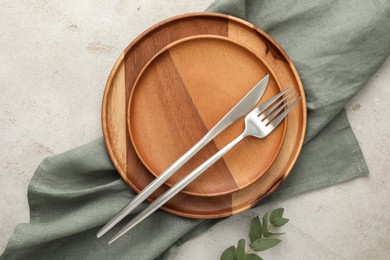 Photo of Stylish setting with cutlery, napkin, eucalyptus branch and plates on light table, top view