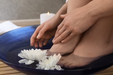 Photo of Woman soaking her feet in bowl with water and flowers on floor, closeup. Spa treatment