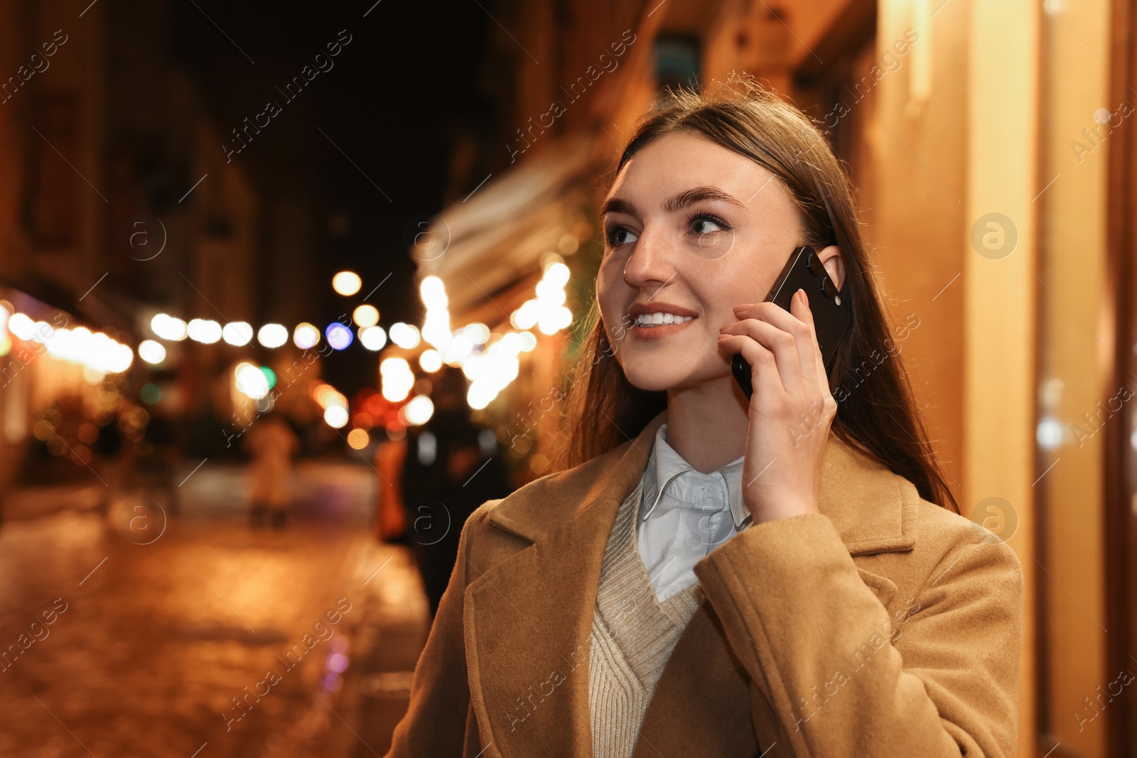 Photo of Smiling woman talking by smartphone on night city street. Space for text