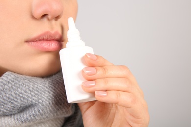 Photo of Woman using nasal spray on light grey background, closeup. Space for text
