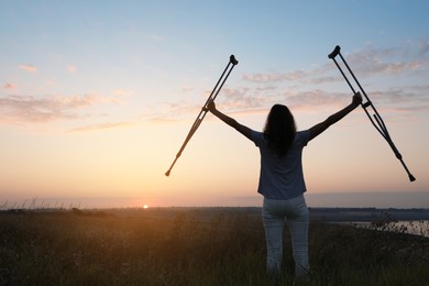 Photo of Woman holding axillary crutches outdoors at sunrise, back view. Healing miracle