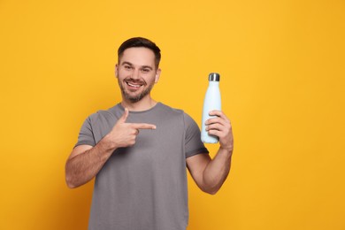 Photo of Happy man pointing on thermo bottle against orange background