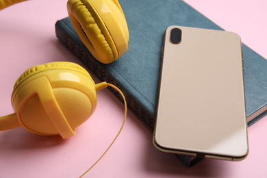 Photo of Book, modern headphones and smartphone on pink background, closeup