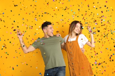 Photo of Happy couple and falling confetti on yellow background