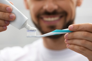 Photo of Man applying toothpaste on brush against blurred background, closeup