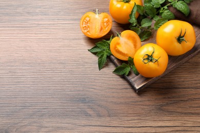 Photo of Fresh ripe yellow tomatoes with leaves on wooden table, flat lay. Space for text