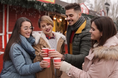 Photo of Happy friends with cups of mulled wine at winter fair
