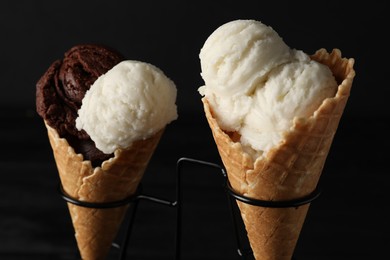 Photo of Ice cream scoops in wafer cones on stand against dark background, closeup
