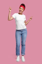 Photo of Happy young woman in stylish headband dancing on pink background