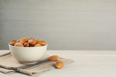 Photo of Ceramic bowl with almonds on white wooden table, space for text. Cooking utensil