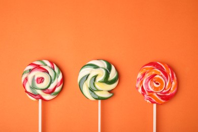 Photo of Colorful lollipops on orange background, flat lay. Space for text