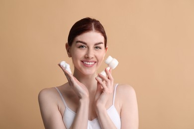 Photo of Washing face. Young woman with brush and cleansing foam on beige background