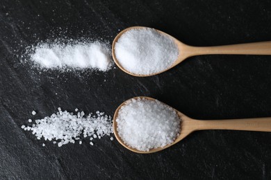 Photo of Organic salt in spoons on black table, flat lay