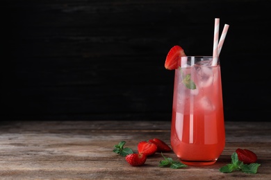 Photo of Glass of refreshing drink with strawberry and mint on wooden table against dark background, space for text