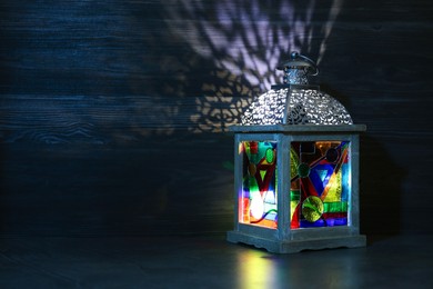 Photo of Decorative Arabic lantern on table against dark background. Space for text