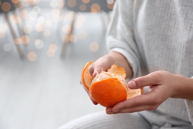 Photo of Woman peeling tangerine on blurred background, closeup. Space for text