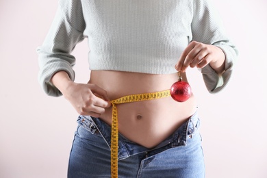 Photo of Woman with Christmas ball and measuring tape on white background, closeup. Overweight problem after New Year party