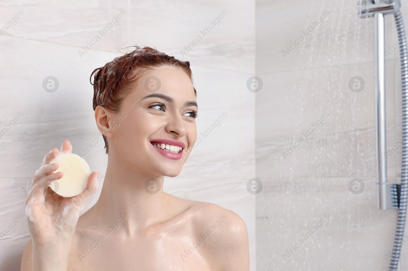 Photo of Happy young woman with solid shampoo bar in shower, space for text