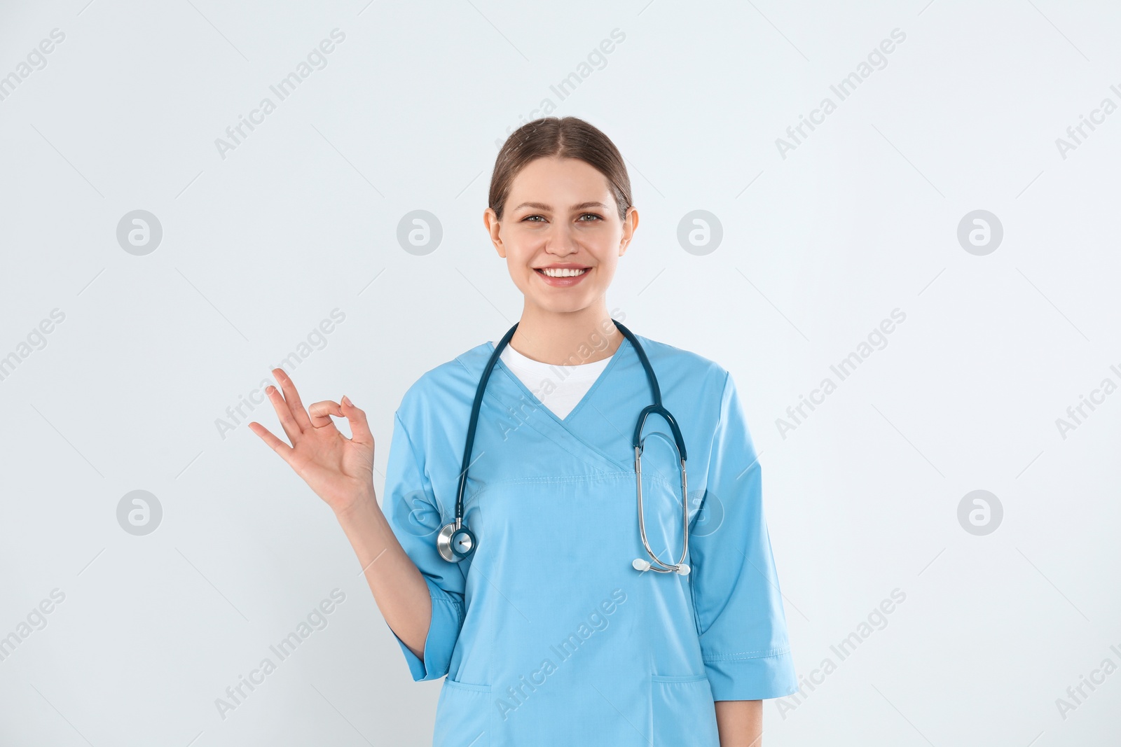 Photo of Young doctor with stethoscope against light background