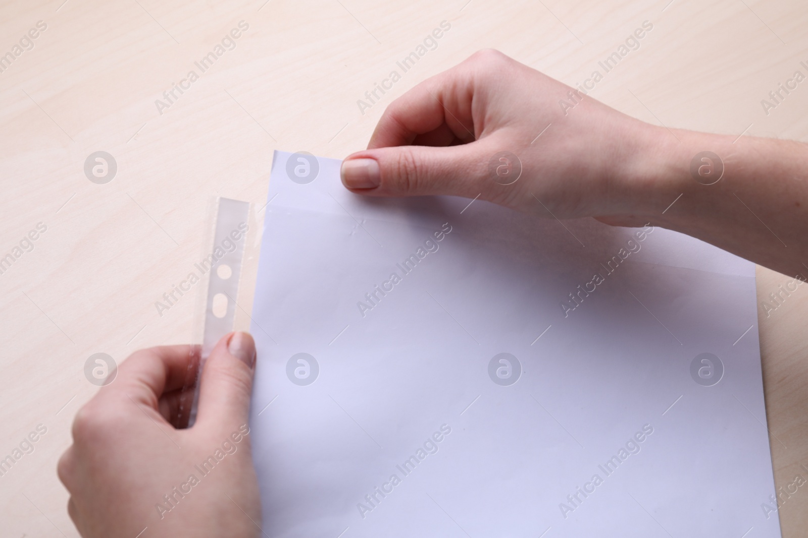 Photo of Woman putting paper sheet in punched pocket at wooden table, closeup