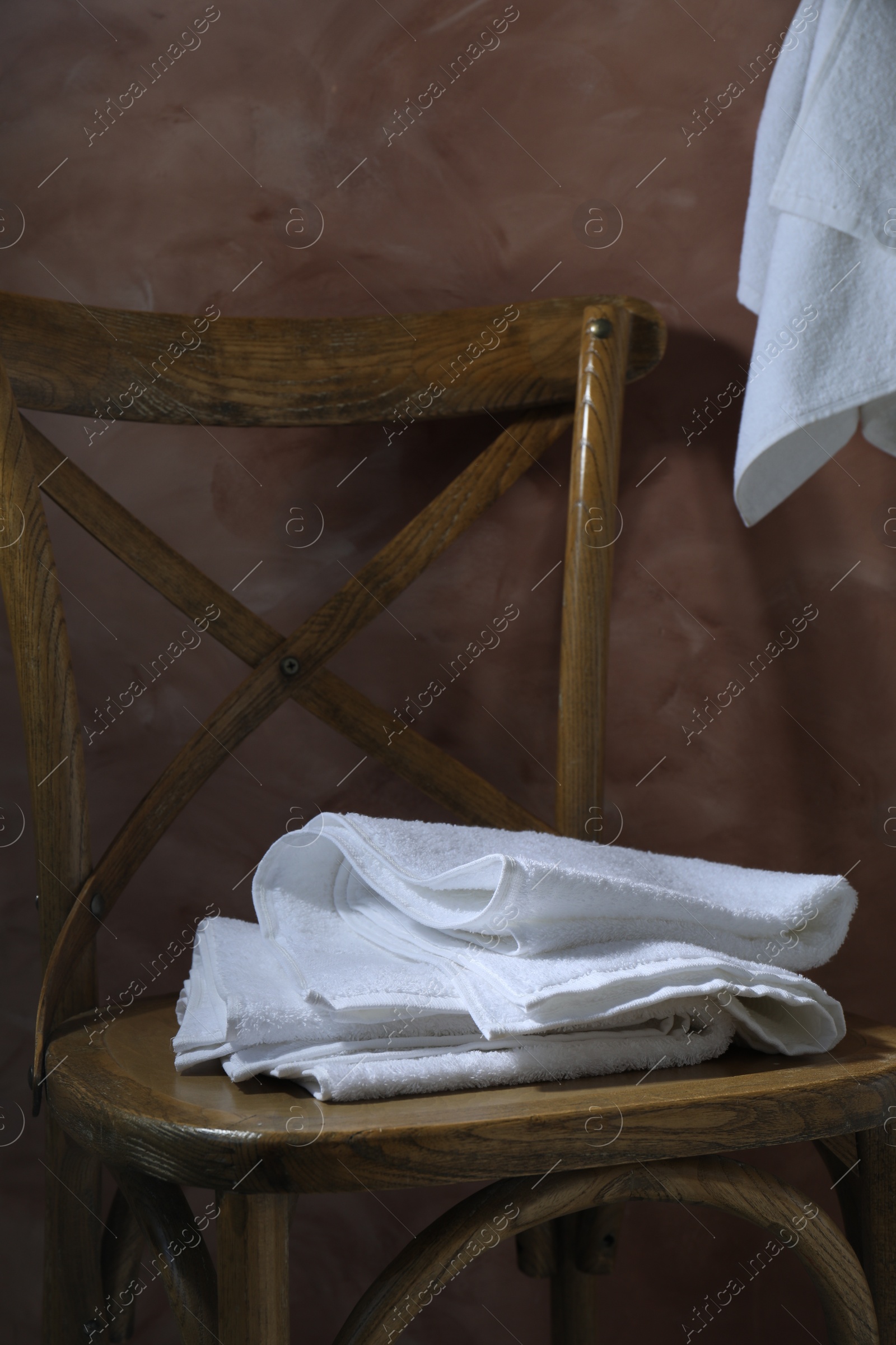 Photo of White terry towels on wooden chair against brown background