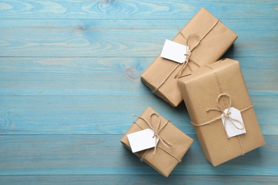 Parcels wrapped in kraft paper with tags on light blue wooden table, flat lay. Space for text