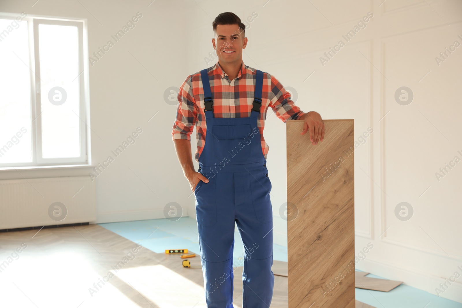 Photo of Professional worker with wooden board indoors. Installing of parquet flooring