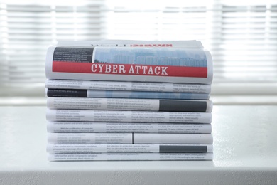 Newspapers with headline CYBER ATTACK stacked on white table indoors