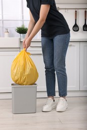 Photo of Woman taking garbage bag out of trash bin in kitchen, closeup