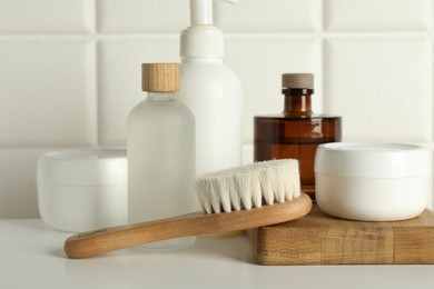 Photo of Bath accessories. Personal care products and wooden brush on white table near tiled wall, closeup