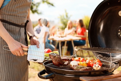 Photo of Man cooking meat and vegetables on barbecue grill outdoors
