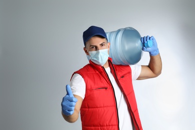 Courier in face mask with bottle of cooler water on grey background, space for text. Delivery during coronavirus quarantine