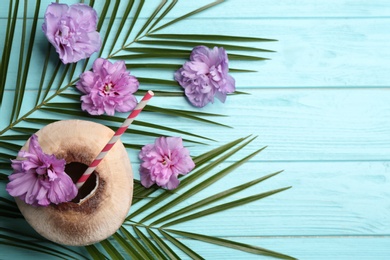 Young peeled coconut with straw, tropical leaves and flowers on light blue wooden table, flat lay. Space for text