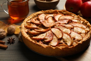 Photo of Delicious apple pie, ingredients and cup of tea on wooden table, closeup