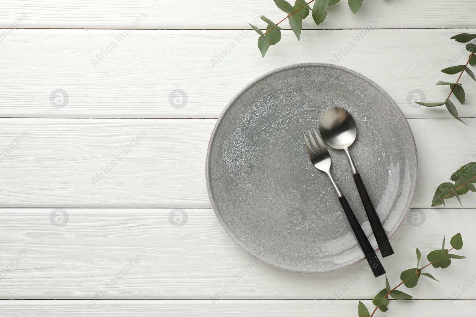 Photo of Stylish setting with cutlery, plate, napkin and eucalyptus branches on white wooden table, top view. Space for text