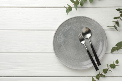 Stylish setting with cutlery, plate, napkin and eucalyptus branches on white wooden table, top view. Space for text