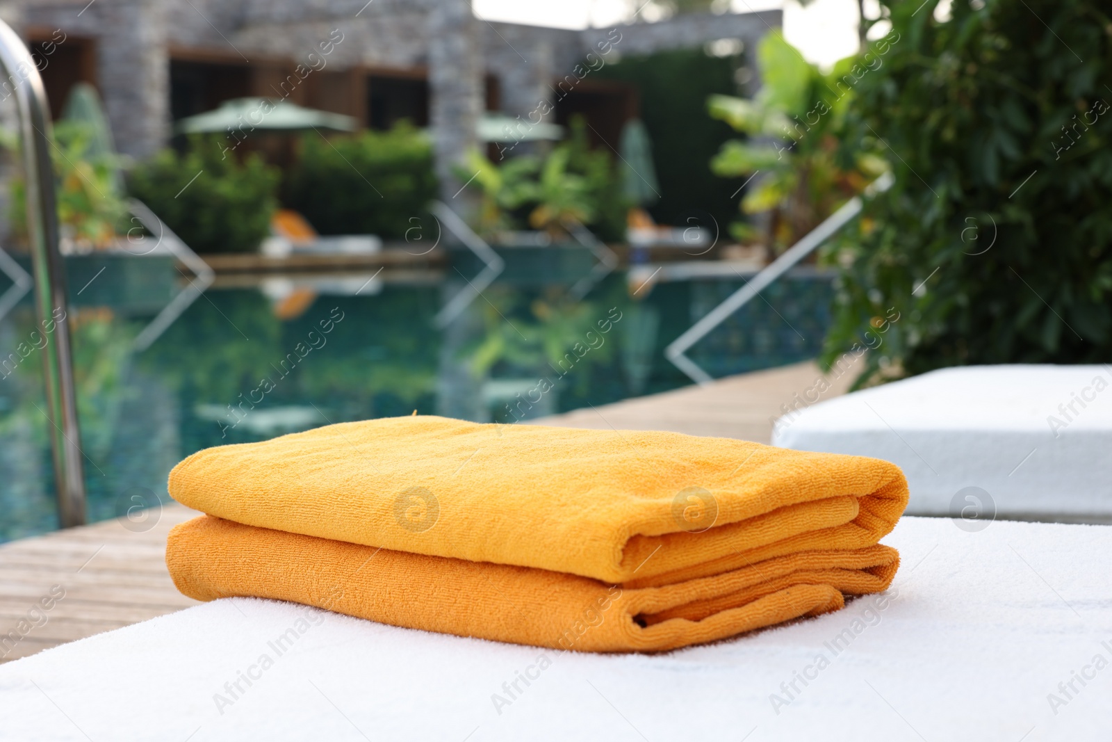 Photo of Beach towels on sun lounger near outdoor swimming pool. Luxury resort