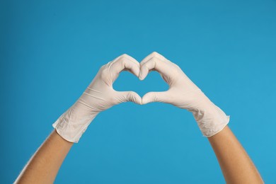 Photo of Doctor in medical gloves showing heart with hands on light blue background, closeup