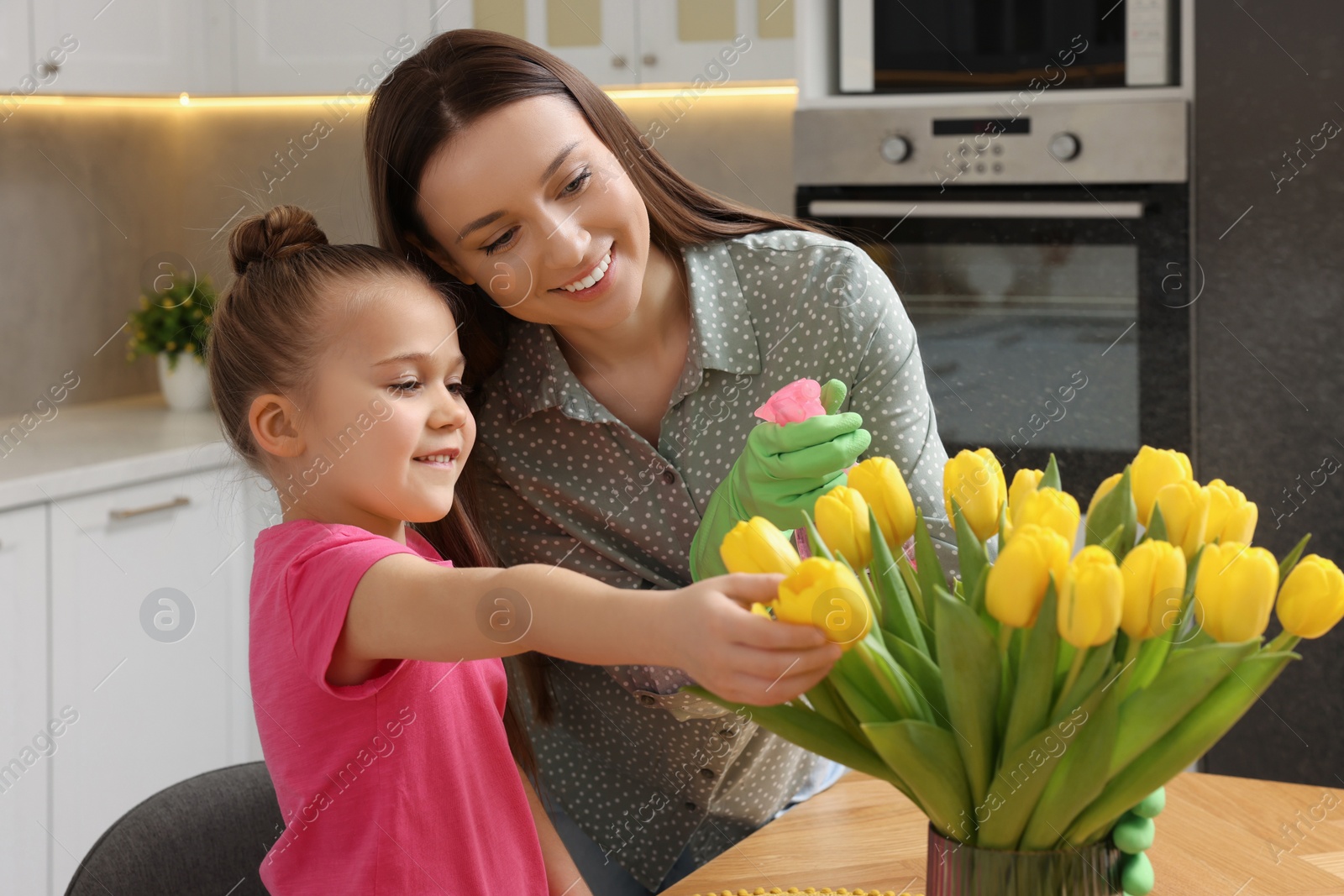 Photo of Spring cleaning. Mother and daughter spraying beautiful bouquet of yellow tulips with water at home