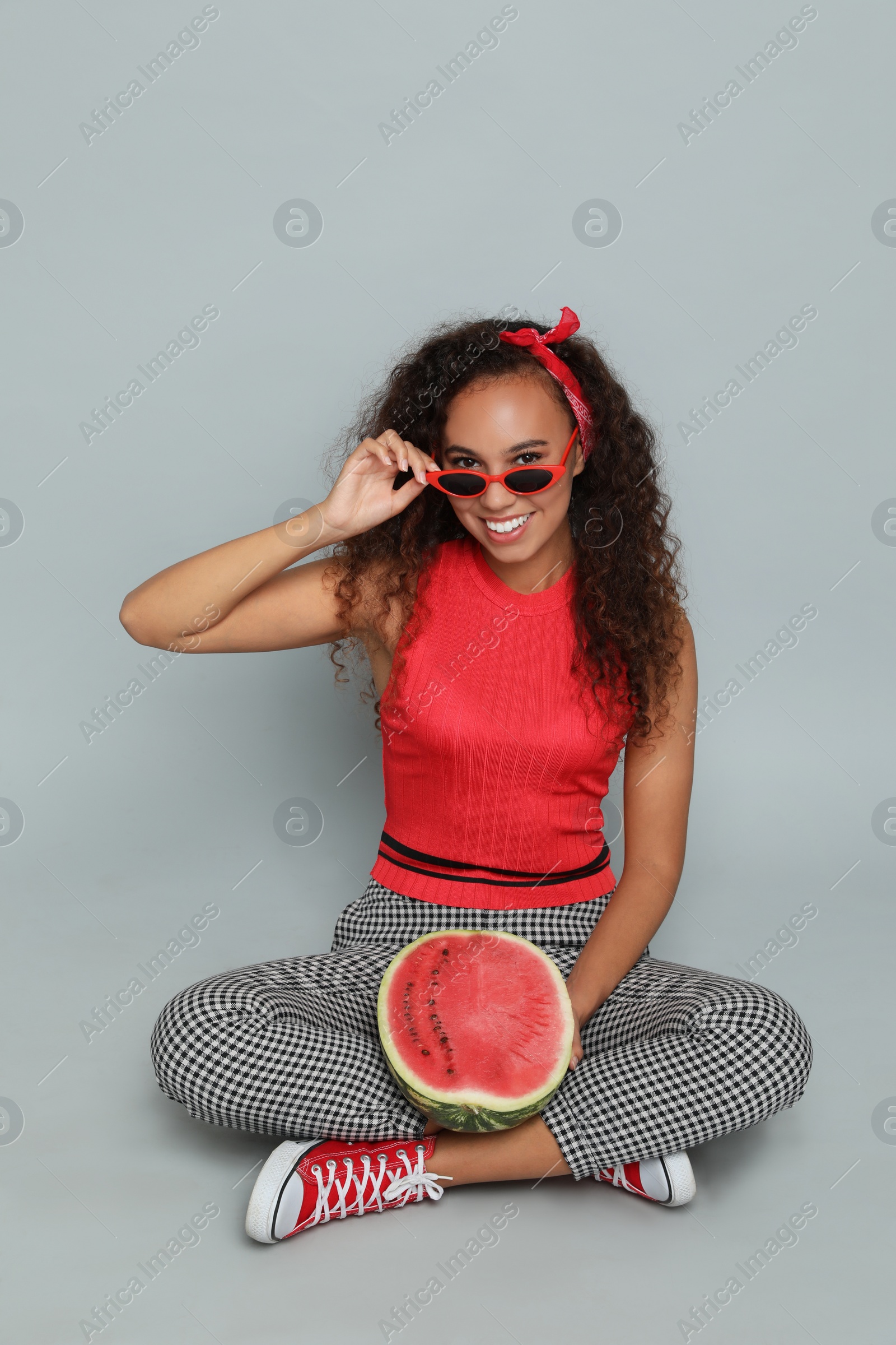 Photo of Beautiful young African American woman with half of watermelon on grey background