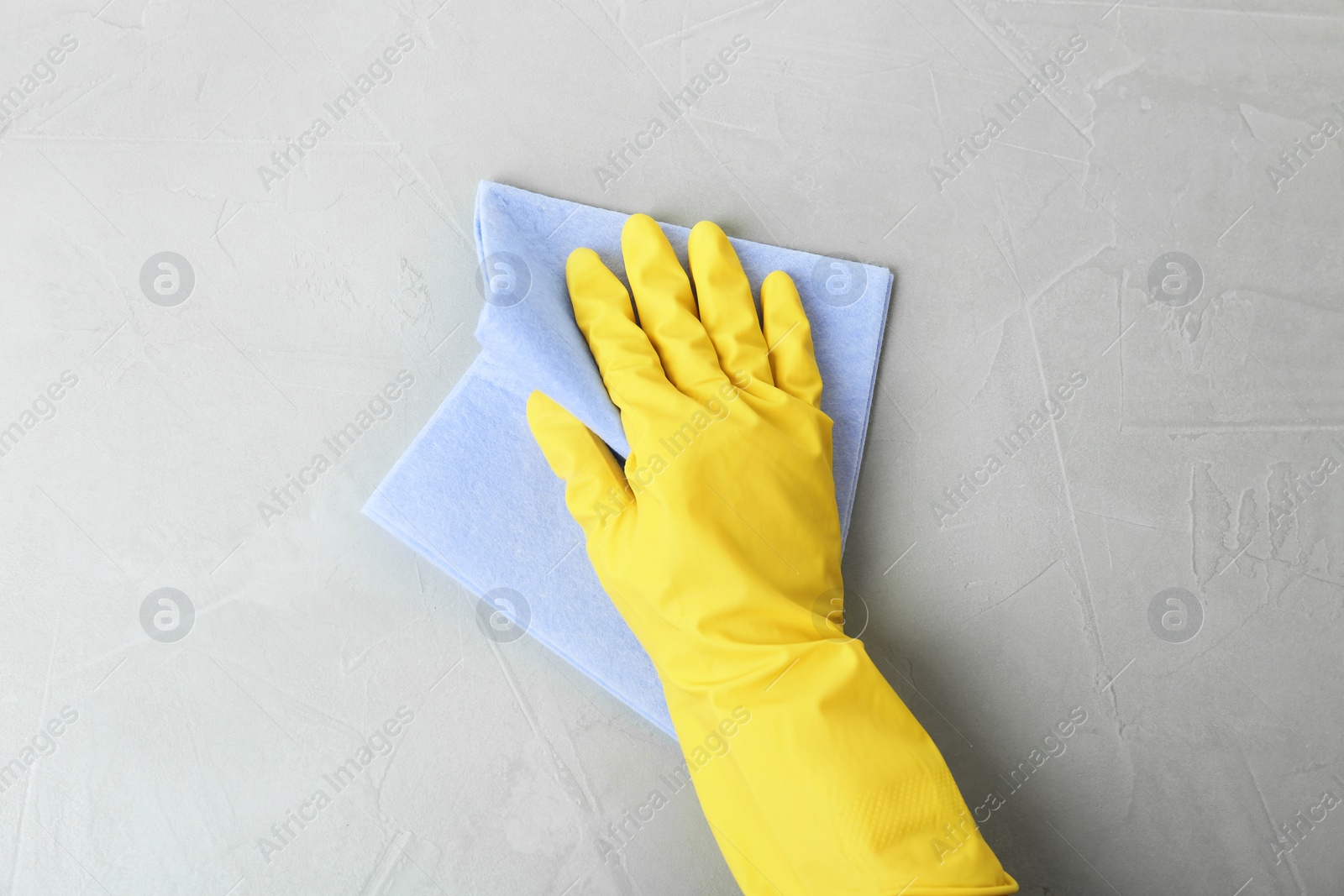 Photo of Person in gloves wiping grey table with rag, top view