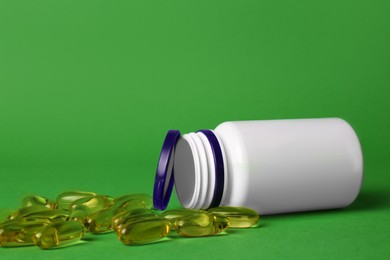 Photo of Plastic medicine bottle and scattered pills on green background, space for text. Medicament