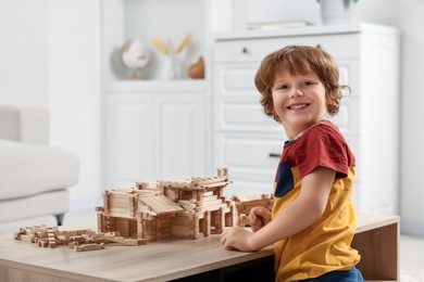 Cute little boy playing with wooden construction set at table in room, space for text. Child's toy