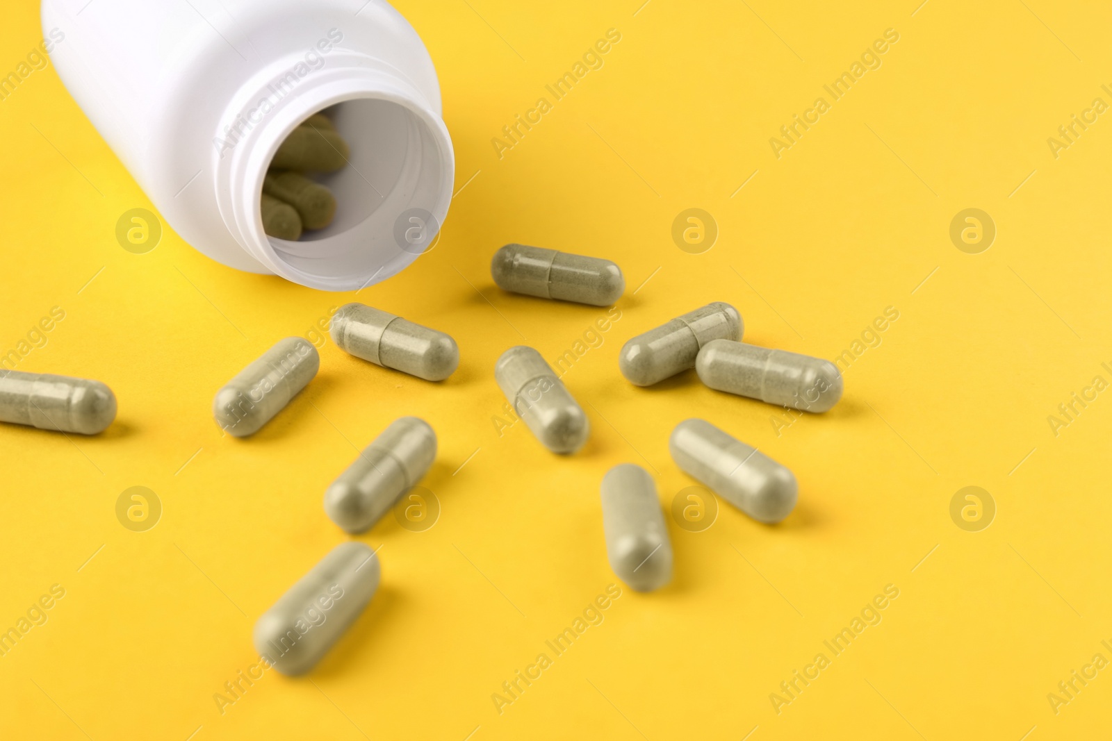 Photo of Bottle and vitamin capsules on yellow background, closeup