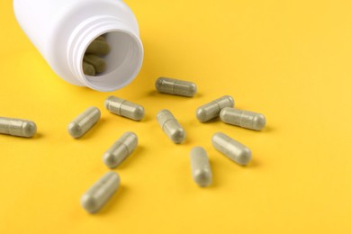 Photo of Bottle and vitamin capsules on yellow background, closeup