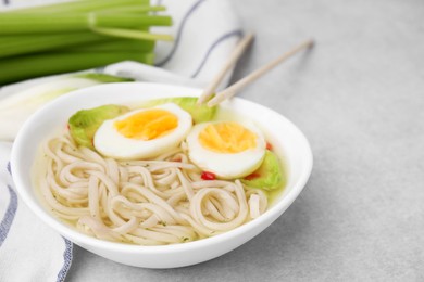 Photo of Bowl of delicious rice noodle soup with celery and egg on light grey table, closeup. Space for text