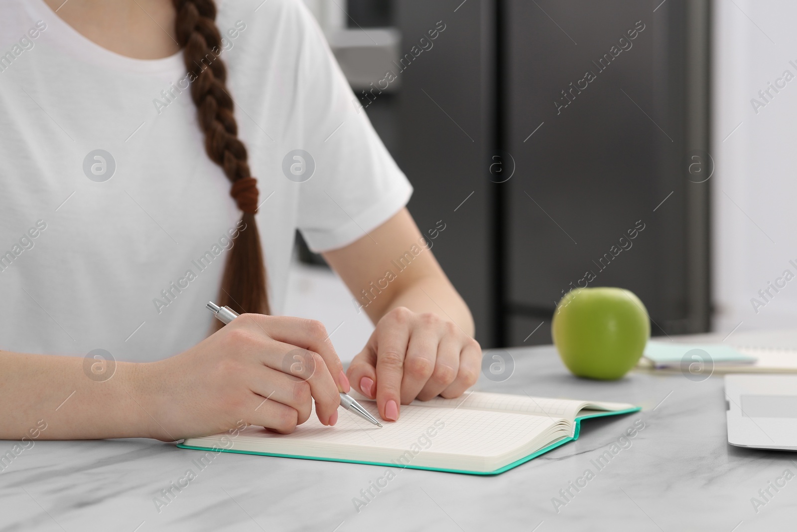 Photo of Woman writing in notebook at white marble table indoors, closeup